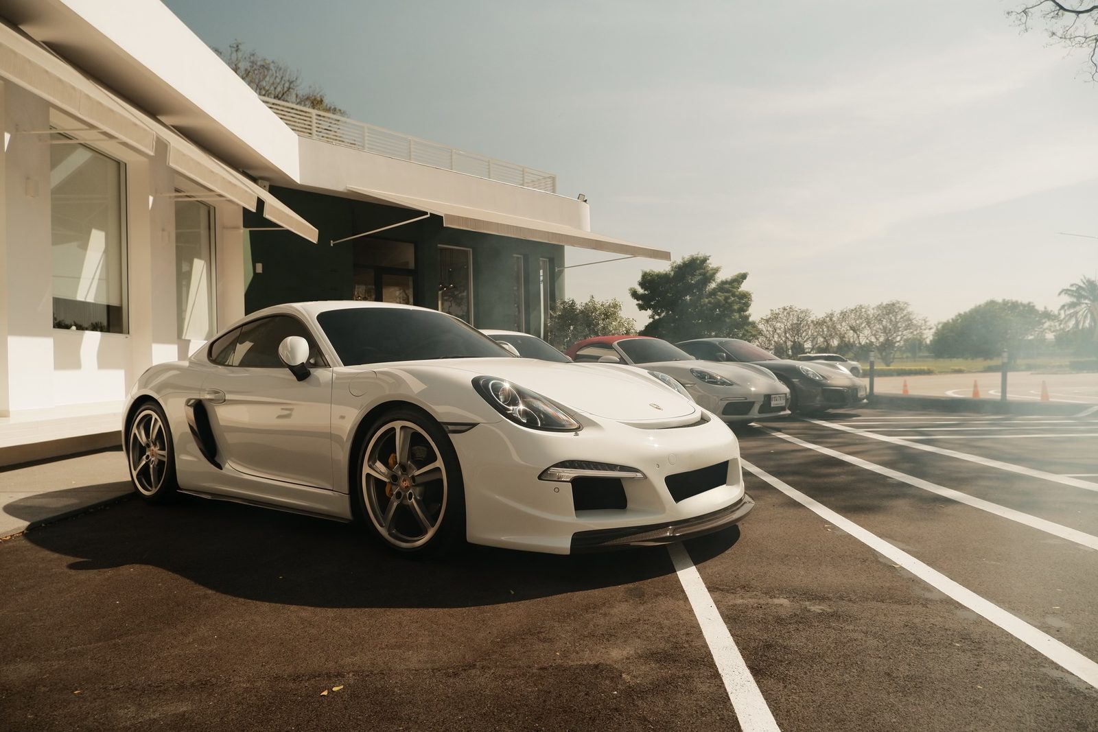 Sports cars lined up outside a white building, smoke drifting across the tarmac